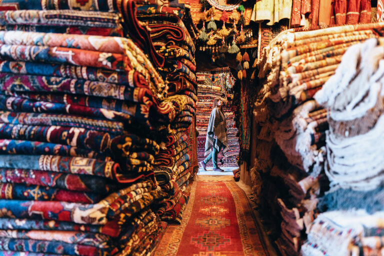 Eine Frau stöbert auf einem Markt in Stapeln von kostbaren Teppichen.