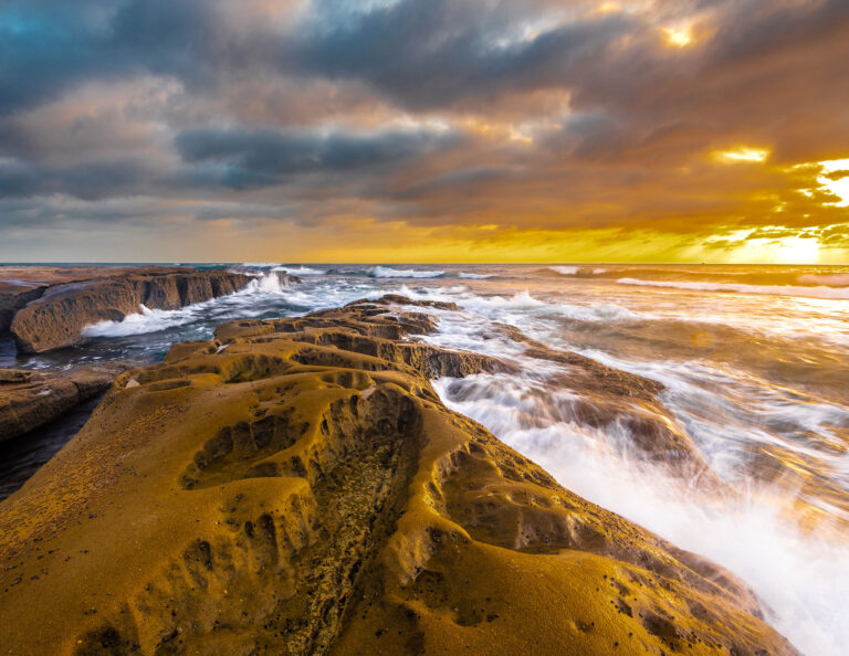 Das Meer plätschert vor einem wolkenverhangenen kalifornischen Himmel auf von der Brandung erodierten Felsen.