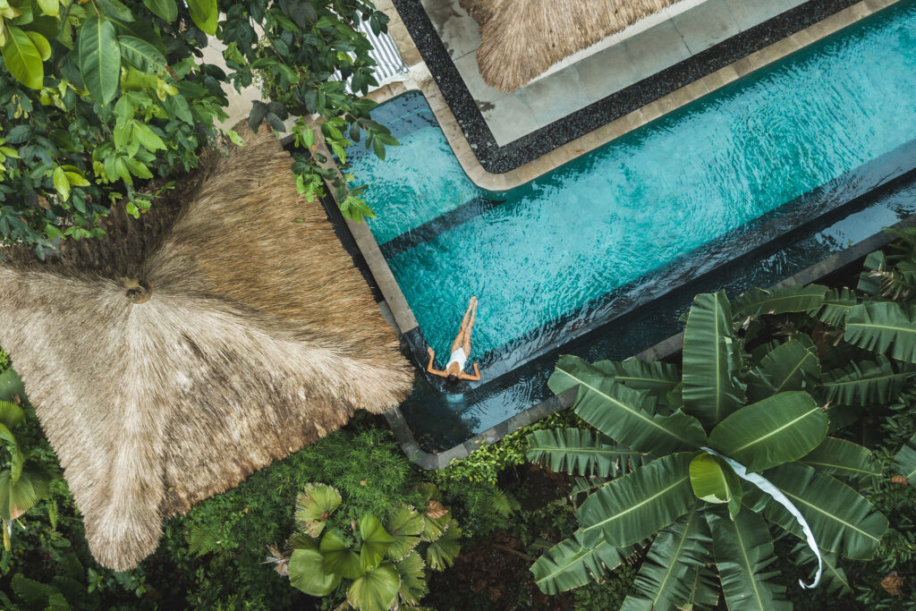 Luftaufnahme einer Frau, die sich in einem Pool inmitten von tropischem Blattwerk entspannt.