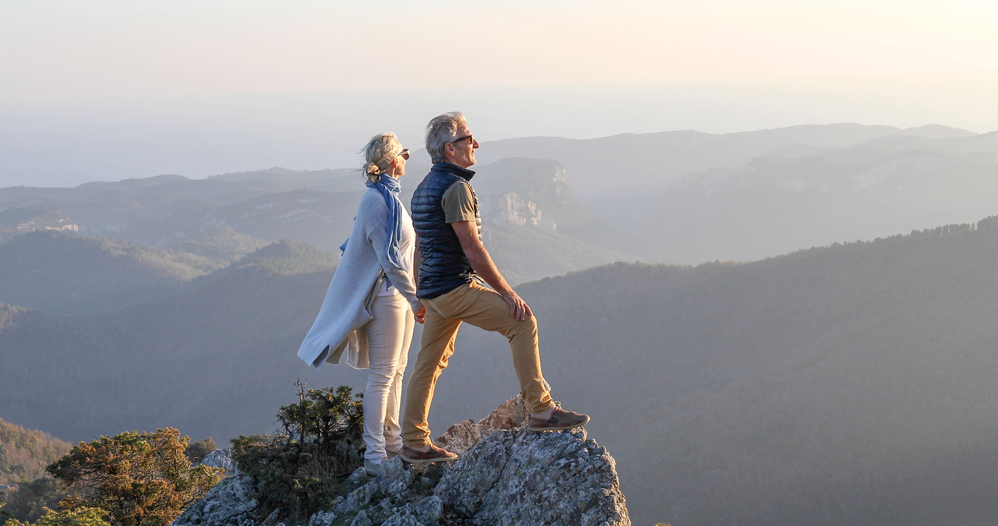 Ein älteres Ehepaar steht auf einem Felsen mit Blick auf die Berge in der Ferne.
