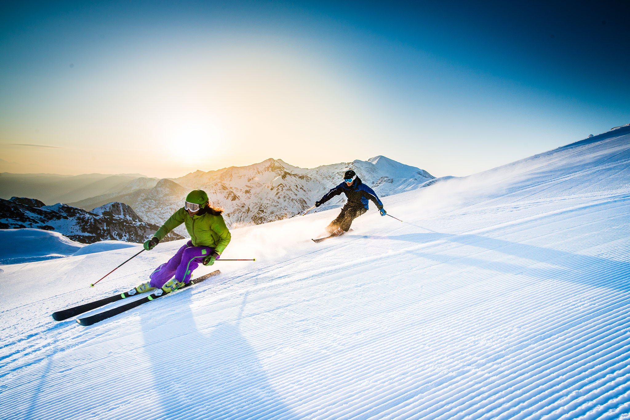 Zwei Skifahrer lehnen sich auf frischem Pulverschnee in eine Kurve.