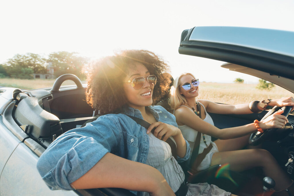 Zwei Frauen sitzen in einem Cabrio und genießen das sonnige Wetter.