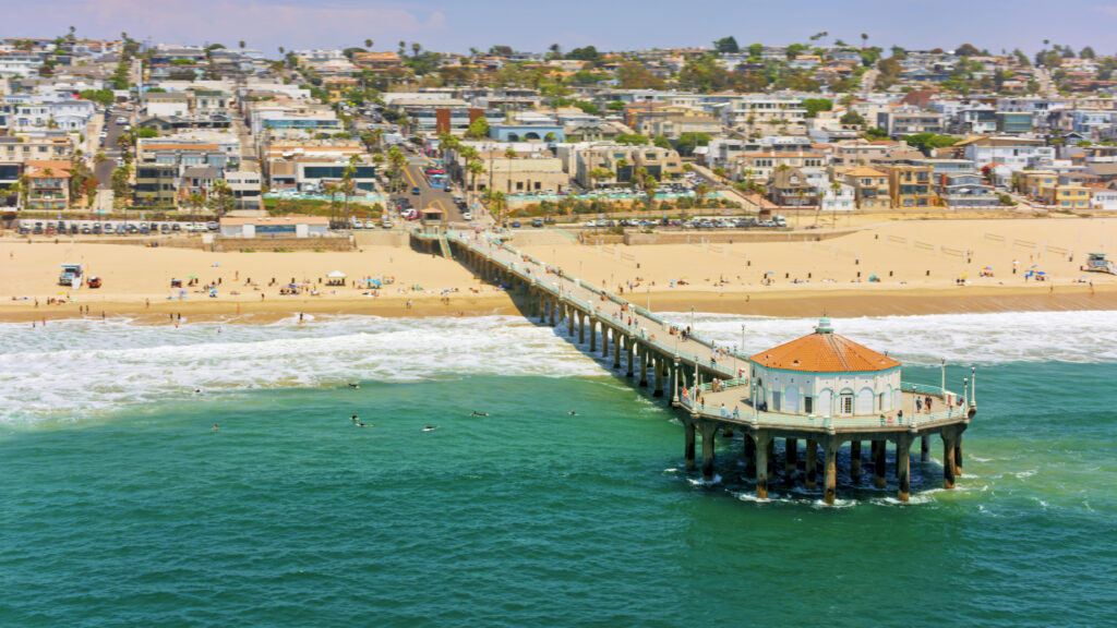 Luftaufnahme des Piers von Huntington Beach und einer Welle, die vor einem Wohnviertel am Strand ausläuft, Orange County, Südkalifornien, Kalifornien, USA.