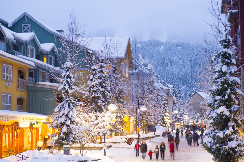 Whistlers Weltklasse-Fußgängerzone mit Geschäften, Hotels und Restaurants, die in der Abenddämmerung mit Neuschnee bedeckt sind